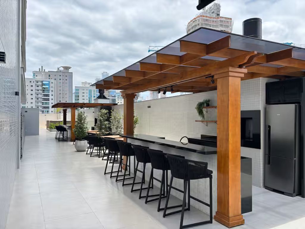 Uma cozinha moderna ao ar livre com área de bar, incluindo um balcão comprido e vários bancos.
