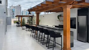 A modern outdoor kitchen with a bar area, including a long counter and multiple bar stools. - Apartment with Sea View • Comfort and Leisure in Itapema (Itapema)