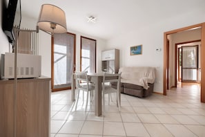 Una sala de estar moderna con una mesa de comedor, sillas, un sofá, una lámpara y un televisor.