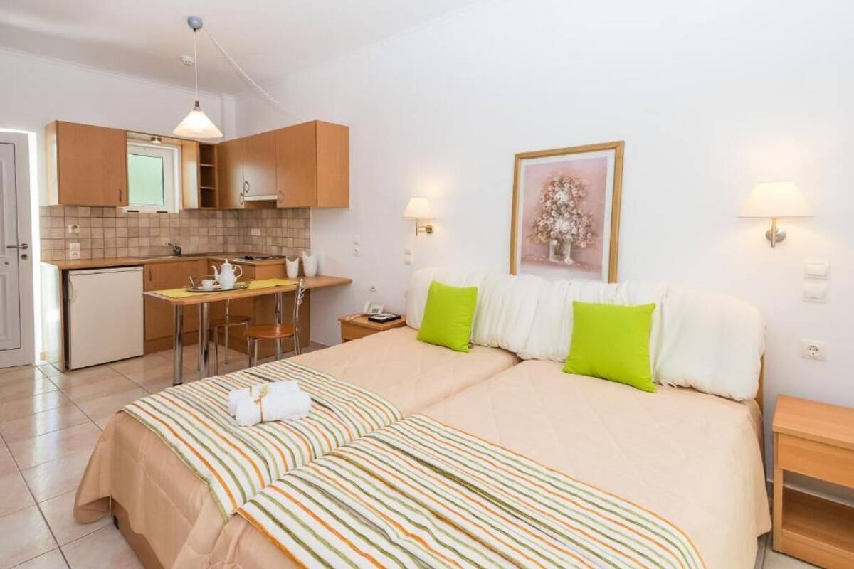 Habitación de hotel con cama, mesita de noche, un escritorio pequeño con silla, kitchenette y un cuadro en la pared.