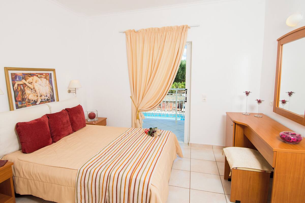 Habitación de hotel con cama, escritorio, espejo, un cuadro y vista a una piscina.