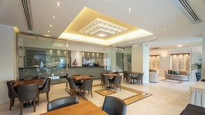 Un moderno vestíbulo de hotel con comedor, mostrador de recepción y zona de estar con sofá y sillones.