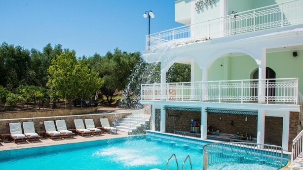 Una piscina con sillones de descanso, zona de bar y un edificio de varios niveles con balcones.