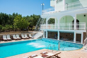 En swimmingpool med liggestole, et barområde og en bygning med flere etager og balkoner.