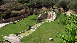 Un puente de piedra, una fuente de agua pequeña y un muro de piedra en un jardín ajardinado.