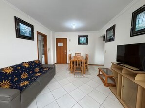 A living room with a sofa, a dining table with chairs, a TV, and framed pictures on the walls. - Ocean view with barbecue, air conditioning and garage. (Itapema)