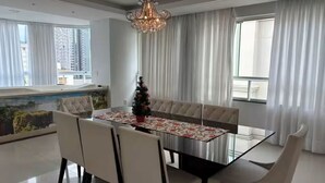 Un comedor con una mesa de cristal, sillas blancas, una lámpara de araña y un árbol de Navidad.