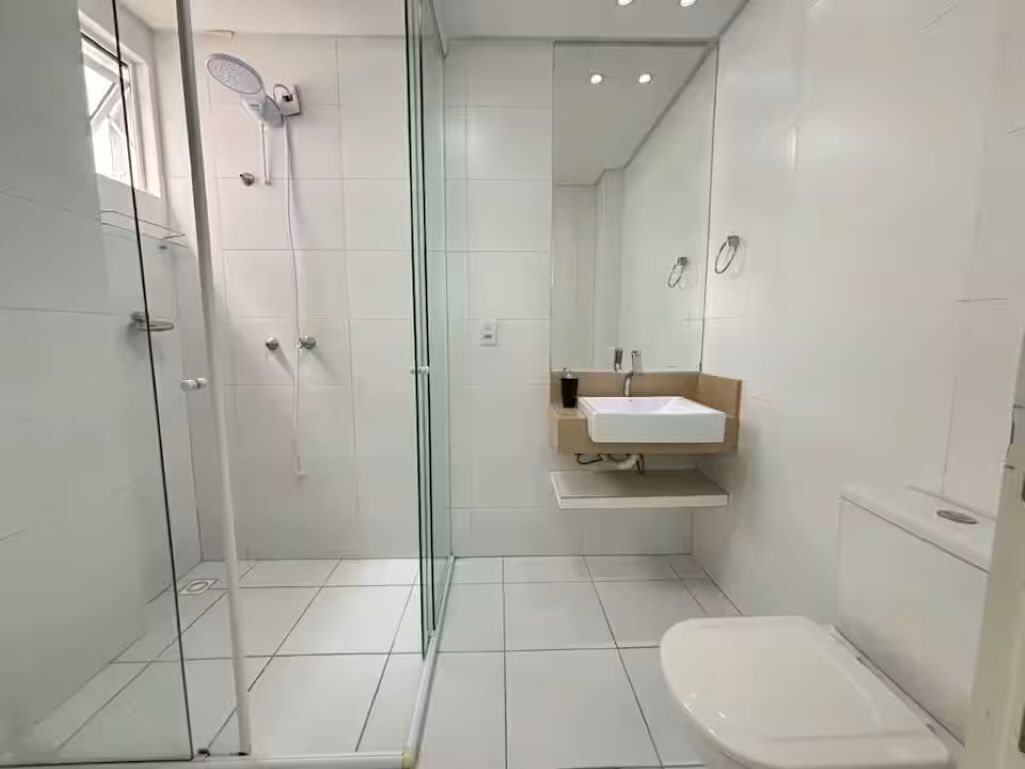 A modern bathroom with a glass-enclosed shower, a white toilet, and a sink with a mirror above it.