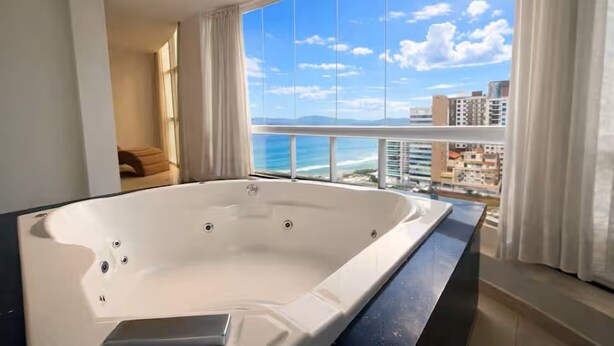 Una bañera blanca grande en una habitación con vistas al océano y edificios.