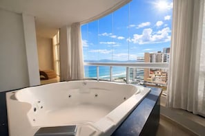A large white bathtub in a room with a view of the ocean and buildings. - Duplex penthouse with a hot tub, grill, and 4 suites (Itapema)