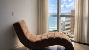 Una sala de estar moderna con un sofá curvo, ventanas amplias y vistas al océano y al paisaje urbano.