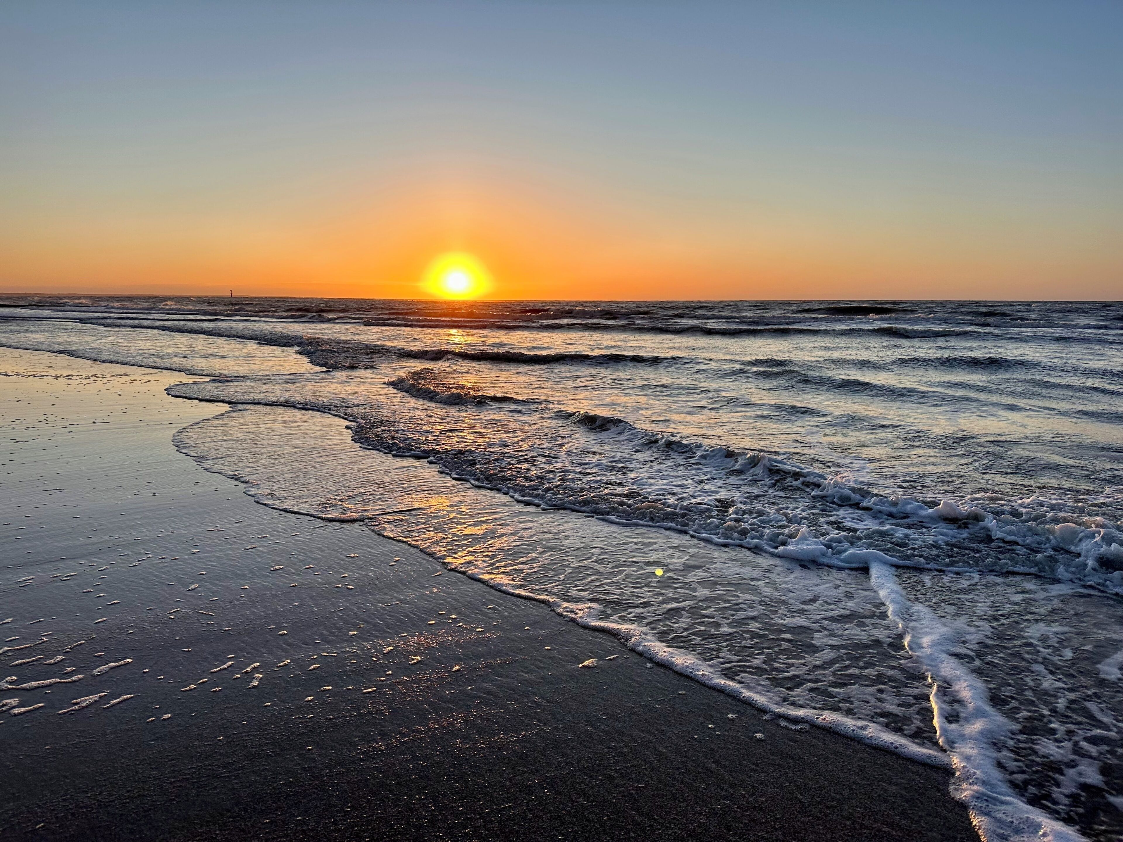 A beach with waves and a sunset.