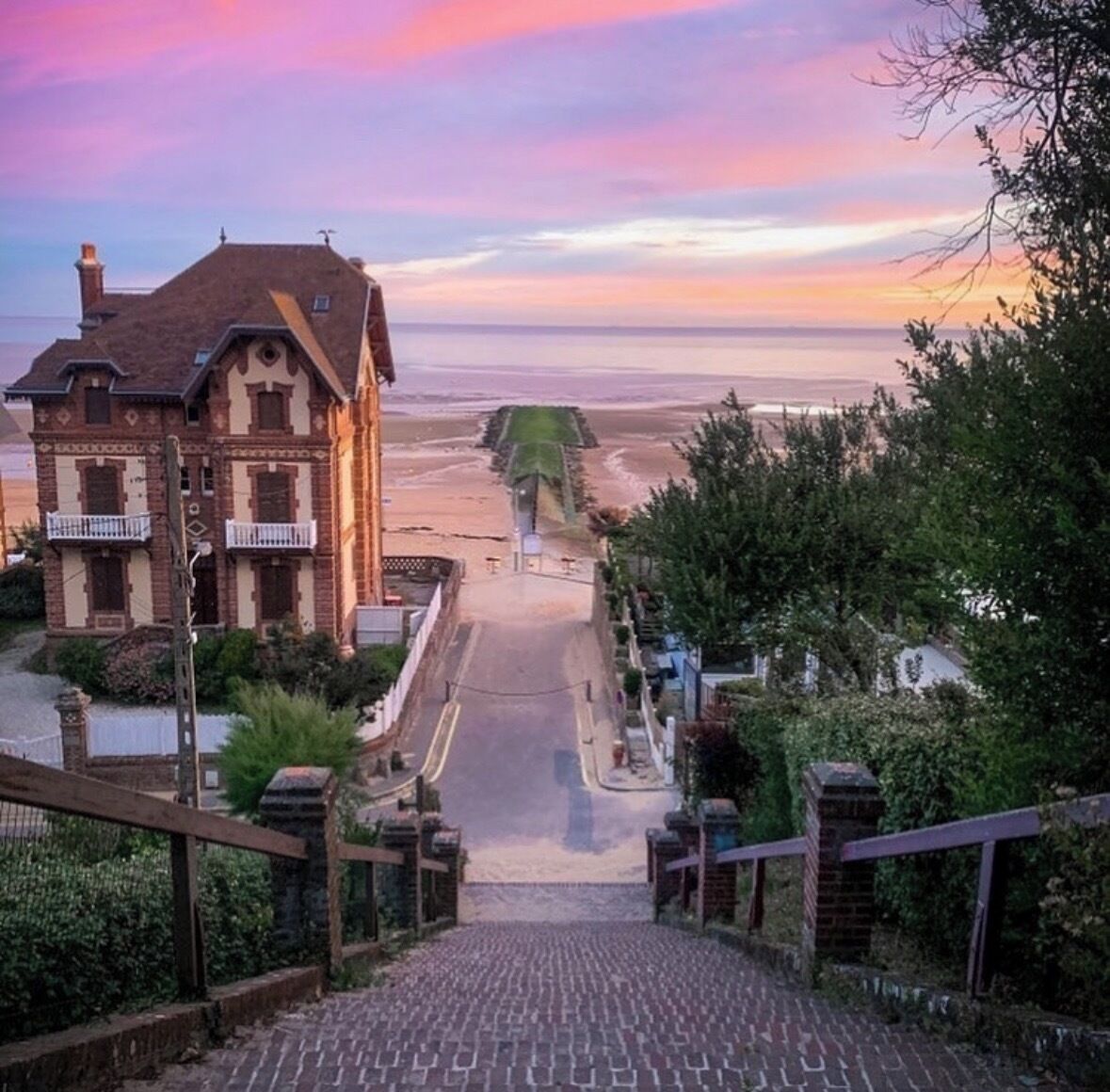 Ein Gebäude mit einer steilen Auffahrt, die zu einem Strand führt, umgeben von viel Grün.