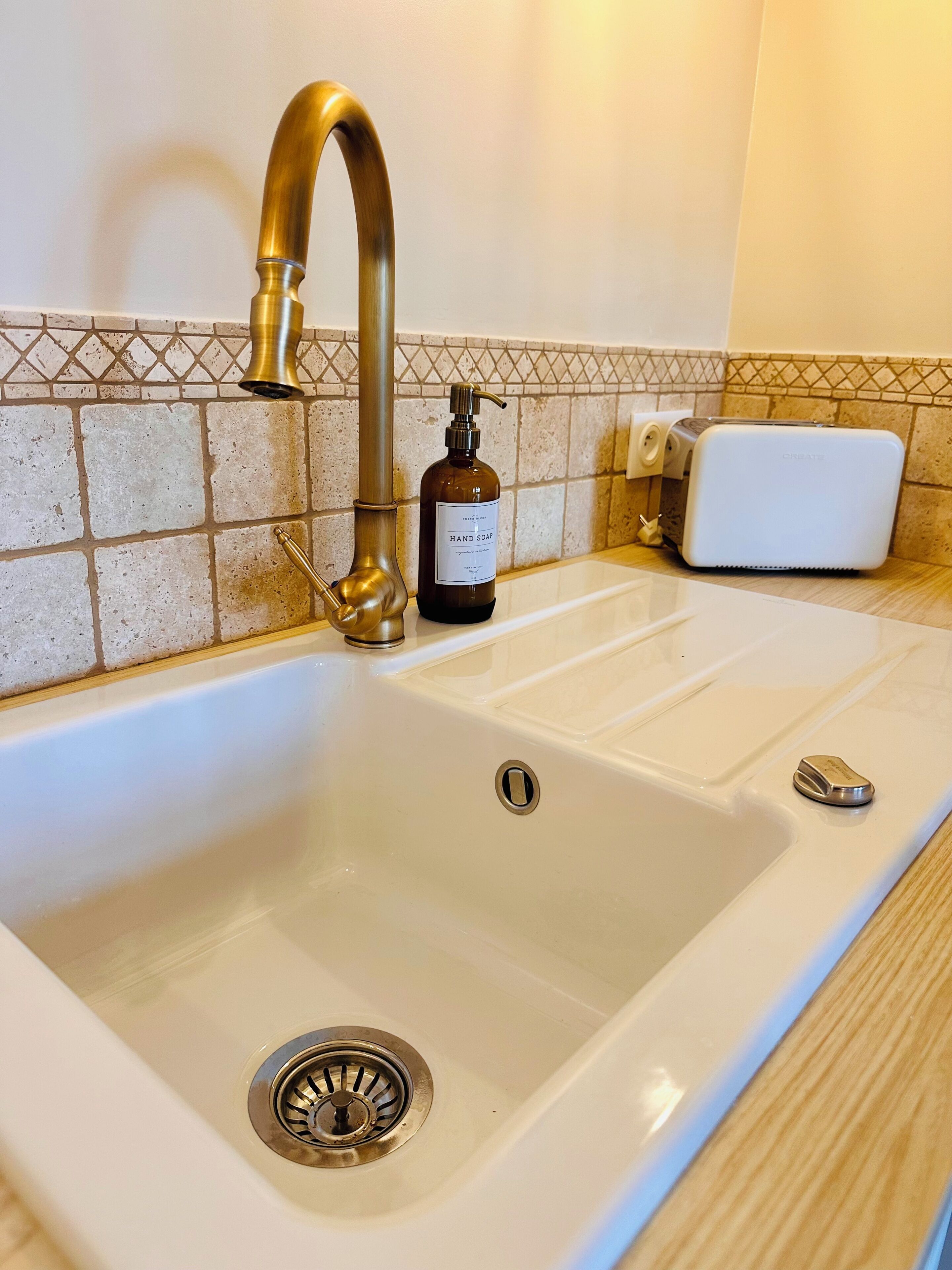 A bathroom sink with a gold faucet, a bottle of hand soap, and a white soap dispenser.