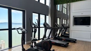 Ett gym med konditionsmaskiner, en tv och stora fönster med utsikt över en sjö eller ett hav.