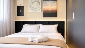 Ett hotellrum med en säng, en sänggavel, en vägg med konstverk och ett kylskåp.