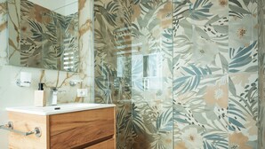 Een badkamer met een houten wastafelmeubel, een spiegel en een douche met deurruitjes met bloemenprint.