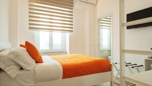 Een slaapkamer met een bed, witte muren, houten vloeren en een raam met zonwering.