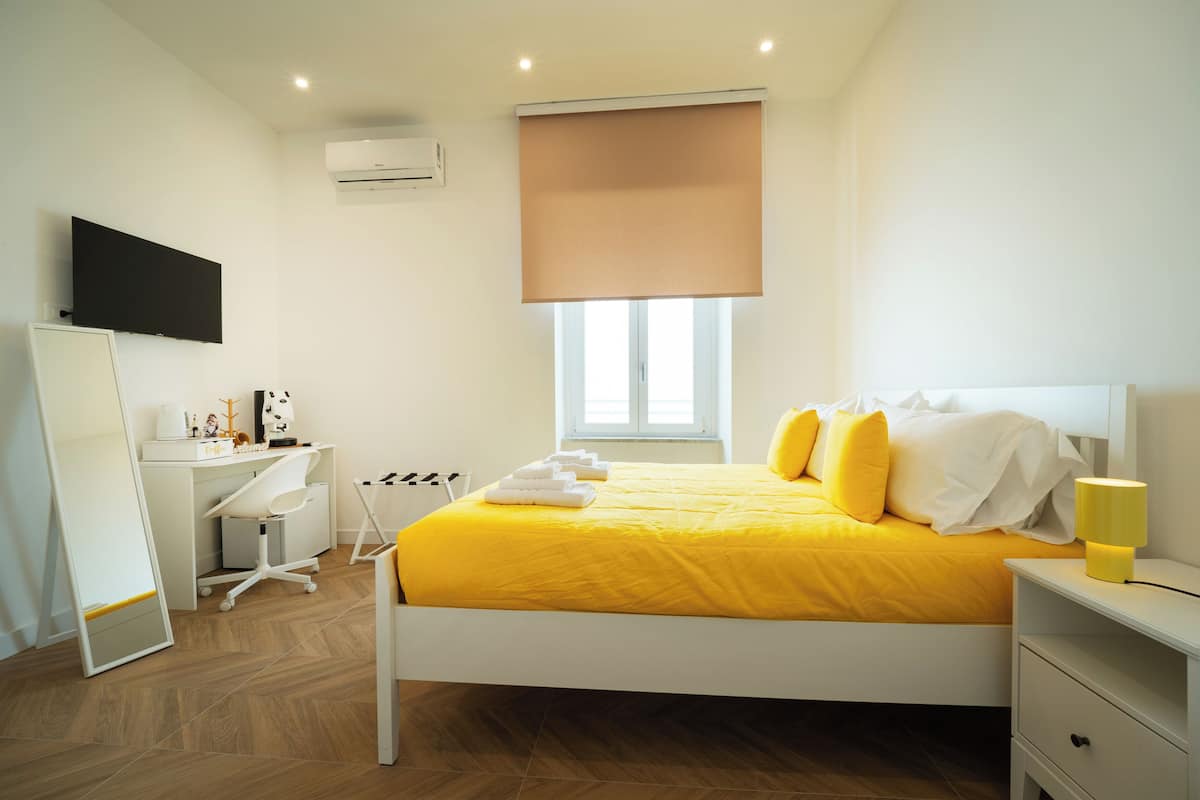 Ein Schlafzimmer mit Bett, Nachttisch, Schreibtisch, Stuhl und Fernseher an der Wand.