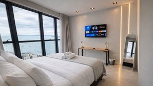 Een moderne hotelkamer met een groot bed, een aan de muur bevestigde televisie en uitzicht op zee.