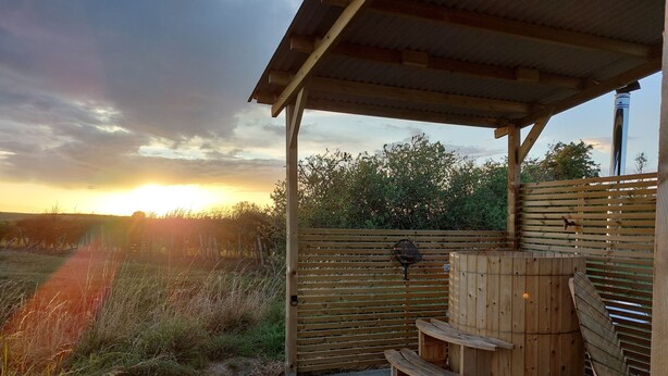 A covered outdoor area with a wooden bench, a grill, and a wooden barrel. - Captain's Cabin Shepherd's Hut with Hot Tub, on the edge of the North York Moors (Pinchinthorpe)