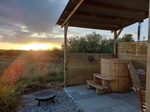 A covered outdoor area with a wooden bench, a grill, and a wooden barrel.