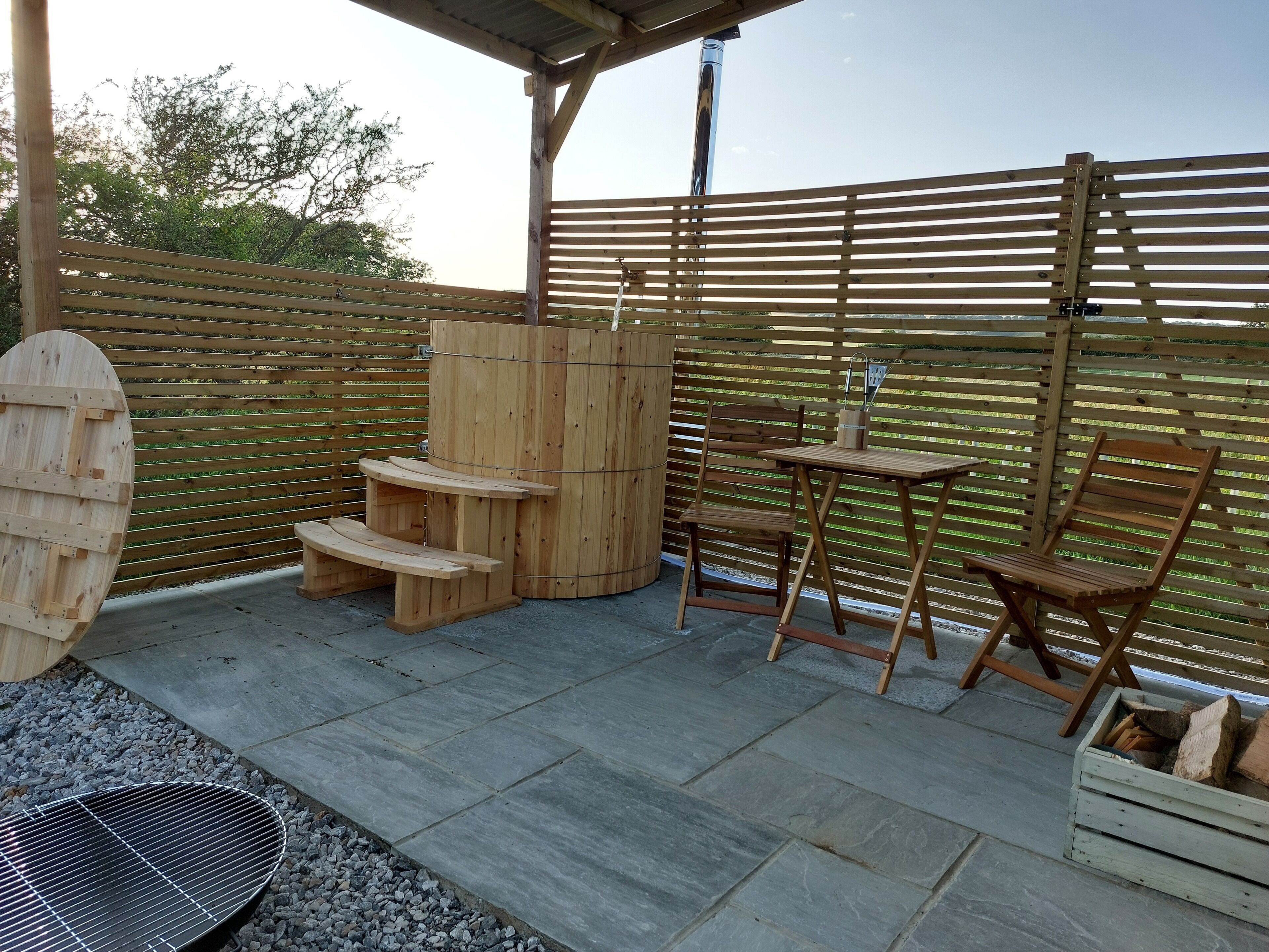 A wooden outdoor seating area with a grill, a wooden table, and chairs.