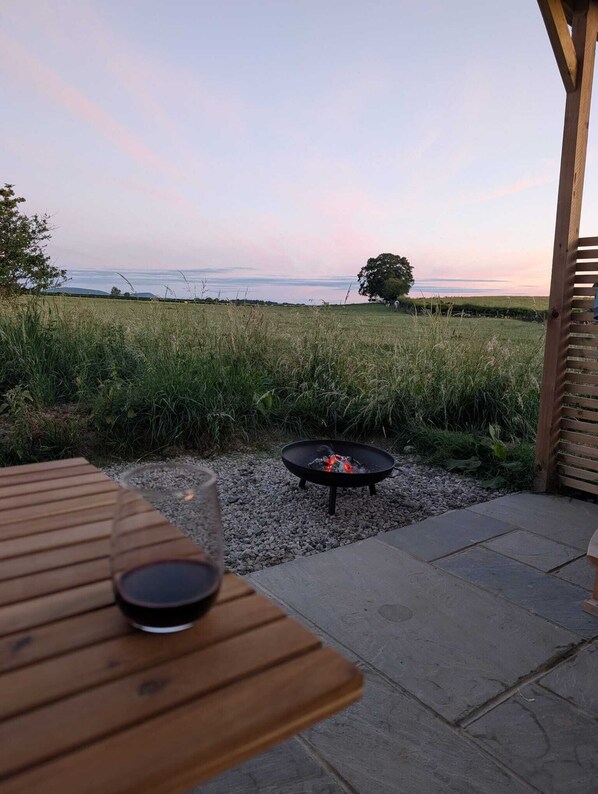 Eine Terrasse im Freien mit einem Feuerkorb, einem Tisch und Blick auf die Landschaft.
