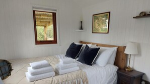 A neatly made bed with folded towels, a wooden headboard, a bedside lamp, a framed world map, and a window with a view of greenery. - Captain's Cabin Shepherd's Hut with Hot Tub, on the edge of the North York Moors (Pinchinthorpe)