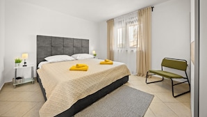 Ein modernes Schlafzimmer mit einem großen Bett, Nachttischen, einer Bank und einem Fenster mit Vorhängen.