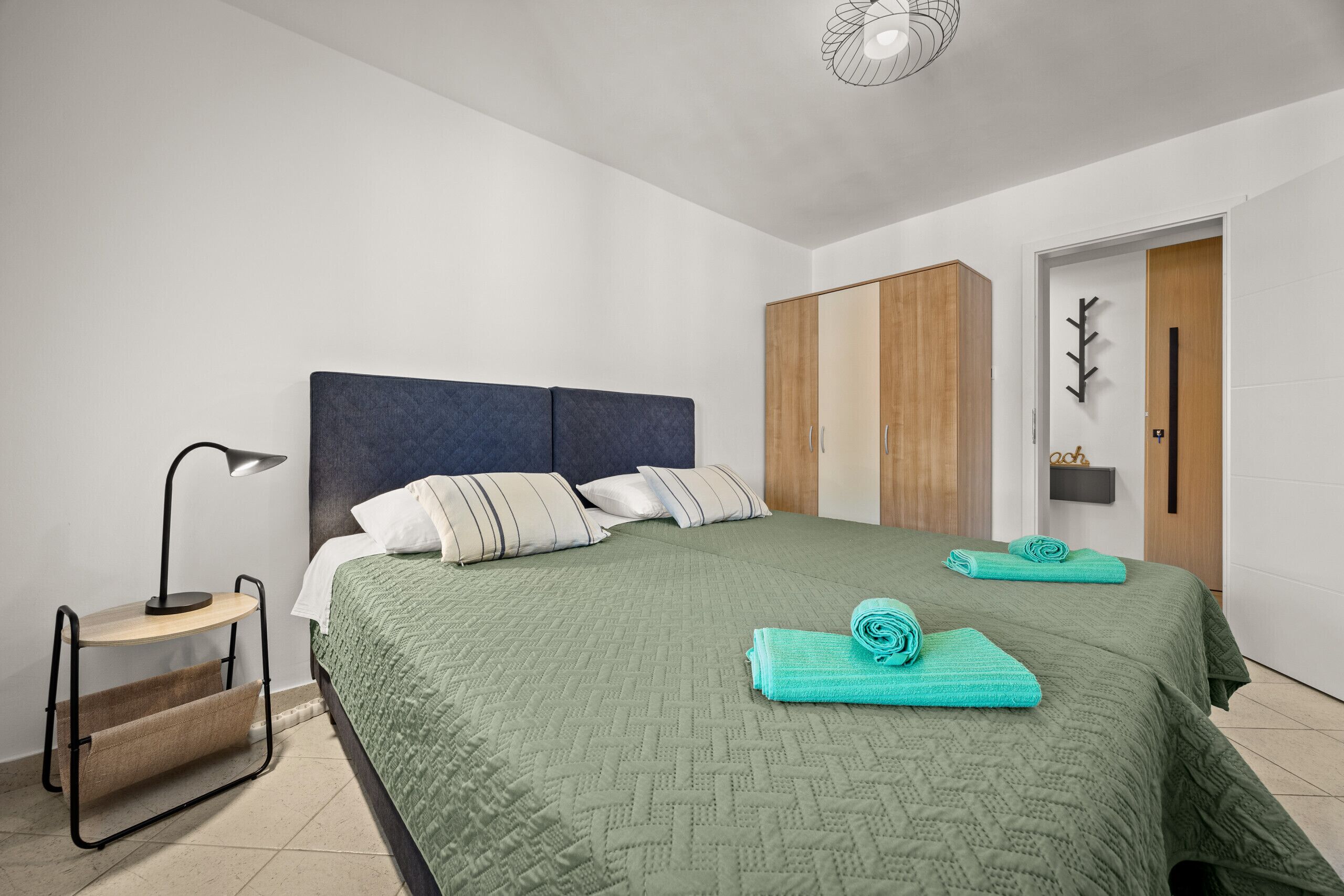 Un lit bien fait, recouvert d’une couette verte, une lampe de chevet et une armoire en bois dans une chambre moderne.