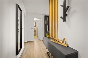 A modern hallway with a wooden floor, a dark console table with a plant, and a wall-mounted light fixture. - Sea Breeze Funtana Apartment A3 (Funtana)