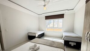 Ein kleiner, sauberer Raum mit zwei Einzelbetten, einem Deckenventilator, einem Fenster und einer Tür.