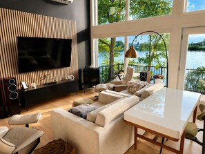 Una sala de estar moderna con un televisor grande, asientos cómodos, una mesa de comedor y vistas a un lago.
