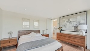 Une chambre à coucher moderne avec un lit, des tables de chevet en bois, une commode et un grand tableau abstrait accroché au mur.