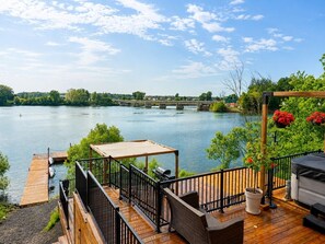 A wooden deck with a grill, a covered table, and a view of a river with a bridge.