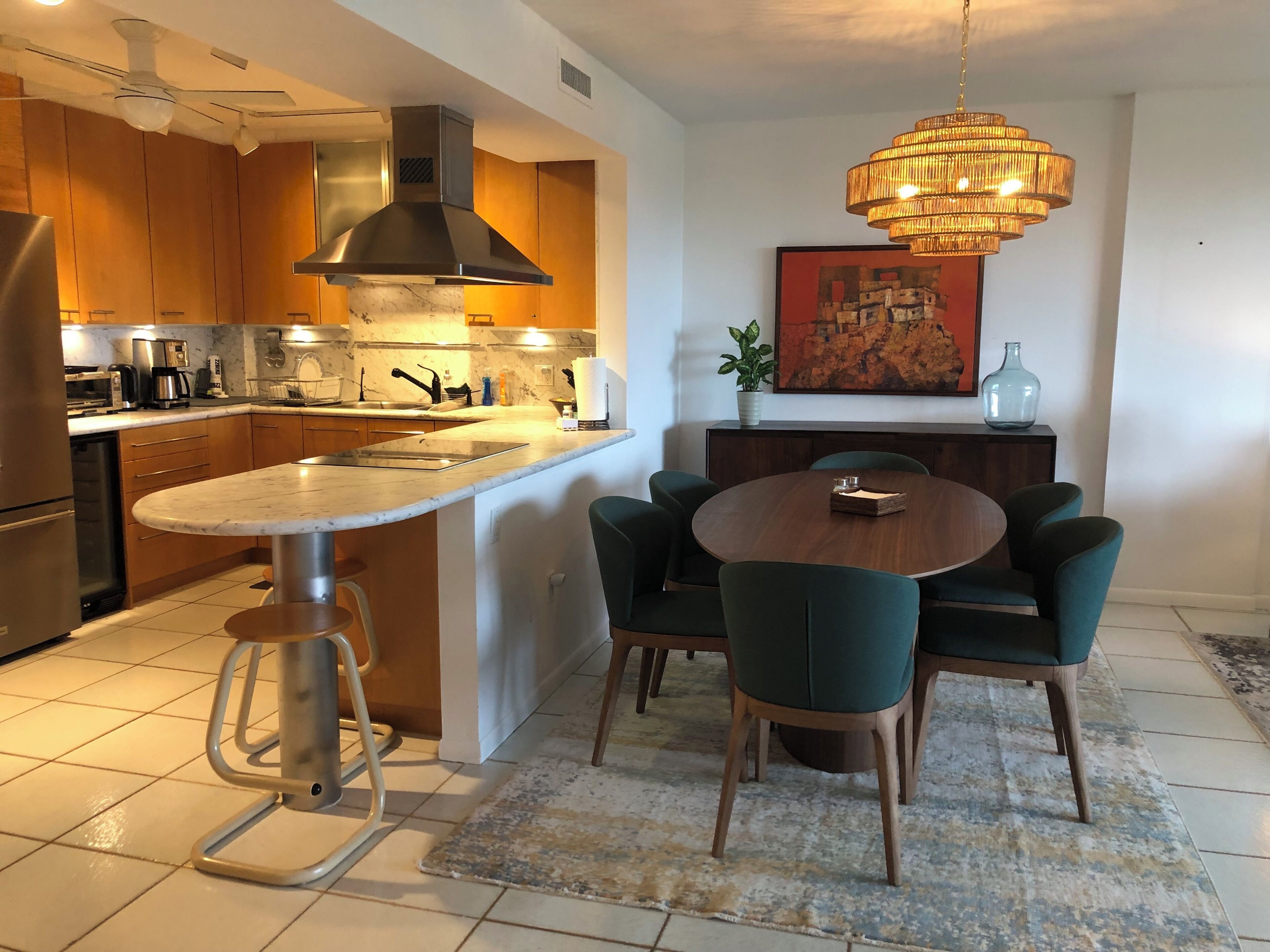 A modern kitchen with a central island, a dining area with a round table and chairs, and a pendant light above.