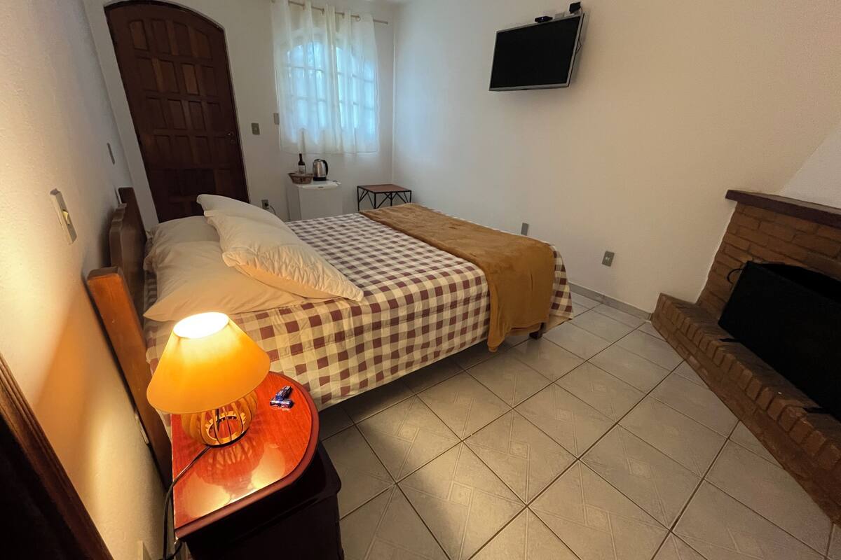 Un dormitorio con una cama, una mesita de noche con lámpara, un televisor en la pared y una chimenea.