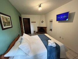 Habitación de hotel con cama, televisor montado en la pared, chimenea y un cuadro enmarcado.