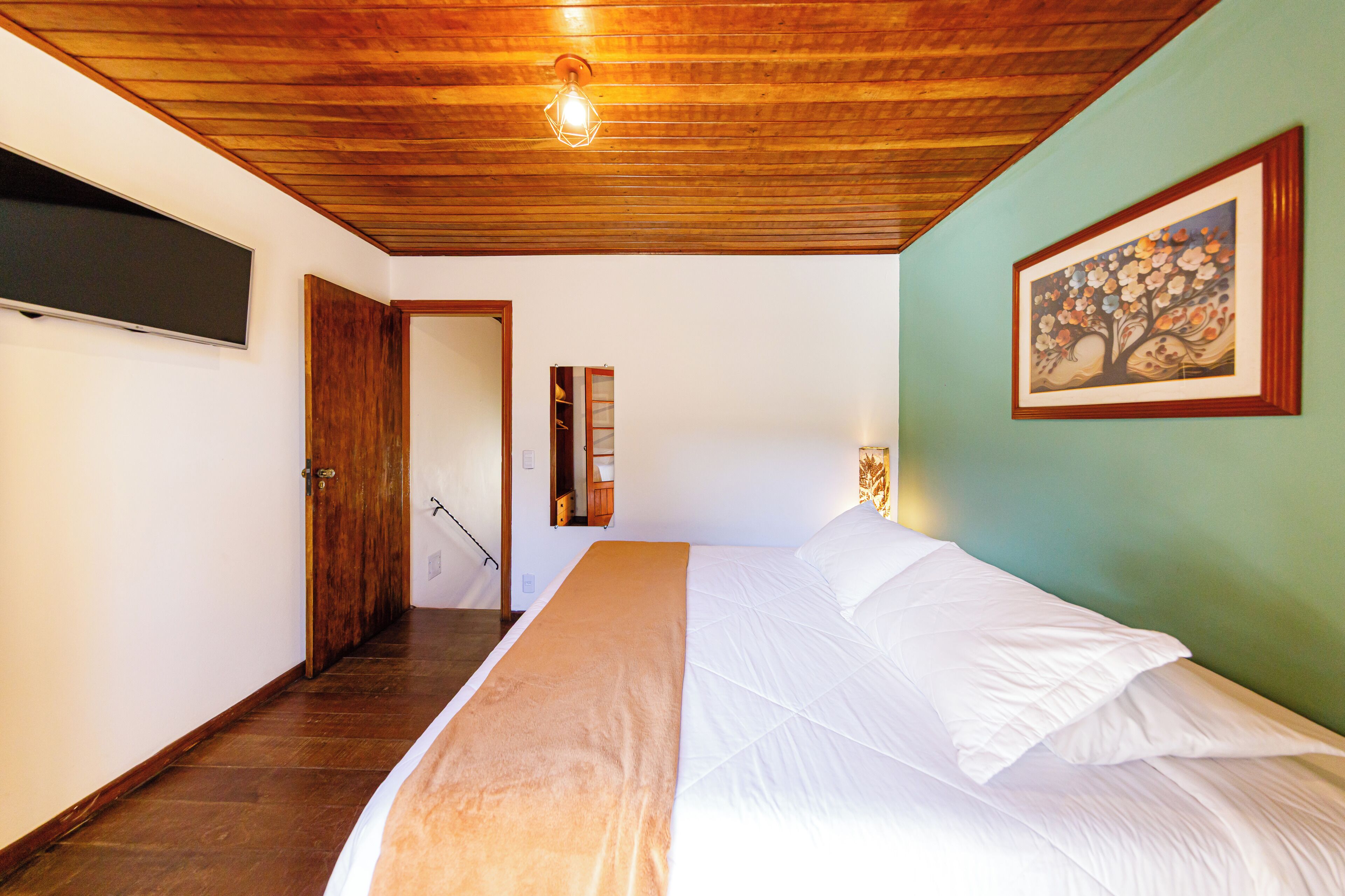 A bedroom with a wooden ceiling, a bed with white linens, a painting on the wall, and a door leading to another room.