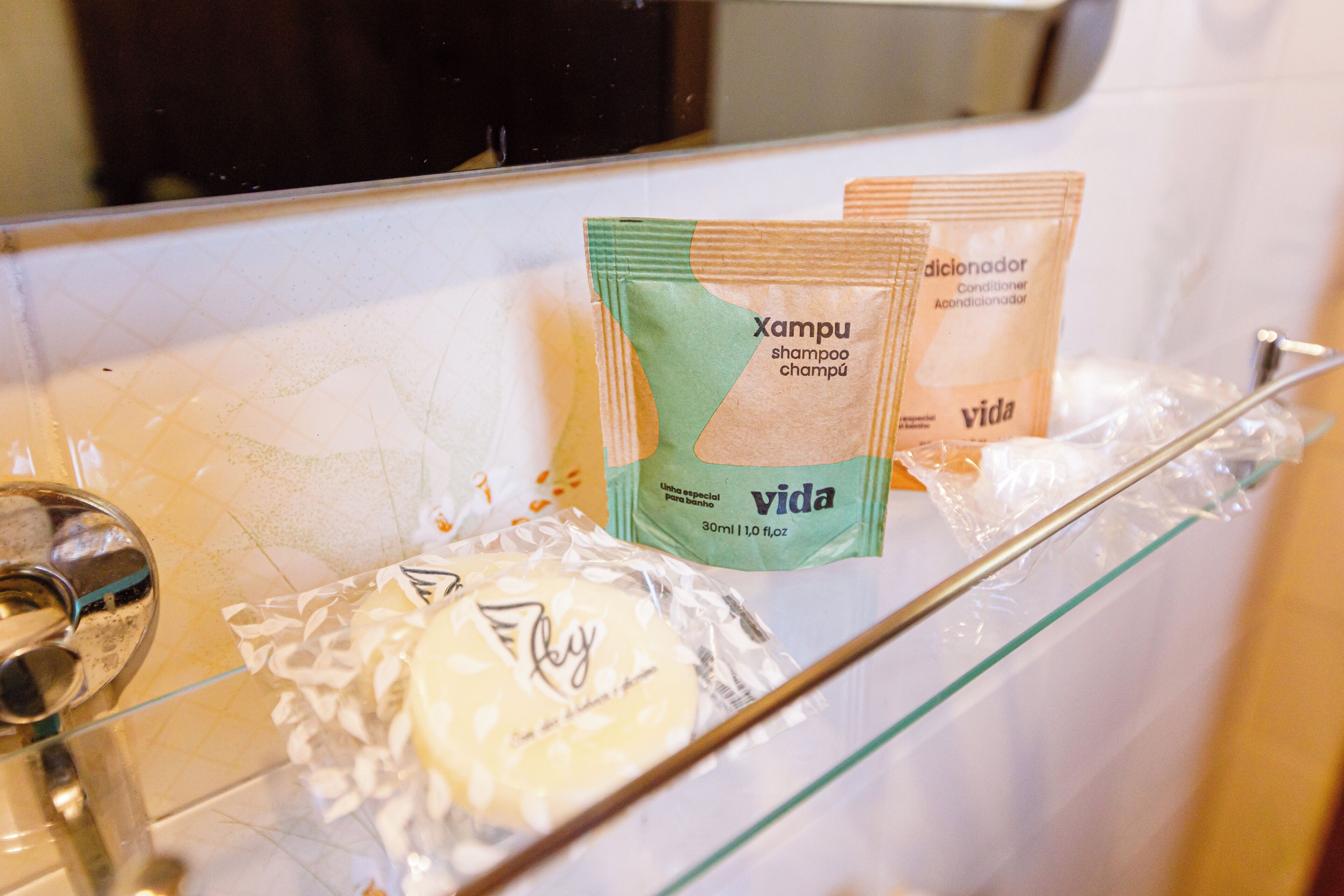 A bathroom with toiletries on a glass shelf, including shampoo and conditioner packets.