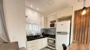 Eine kompakte Küche mit weißen Schränken, einer Mikrowelle, einem Kühlschrank, einem Esstisch mit Stühlen und einer Wand mit Holzverkleidung.