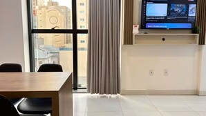 Ein modernes Hotelzimmer mit großem Fenster, einem flachbildfernseher an der Wand, einem Holztisch und einem Sessel.
