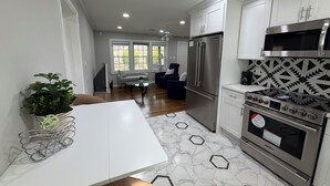 Een moderne keuken met een roestvrijstalen koelkast, oven en magnetron, een eethoek met een witte tafel, en een woonkamer met een bank en een televisie.