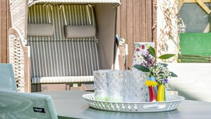 En terrasse med en stribet stol, et bord med en bakke med en vase og blomster, samt en dekorativ kande.