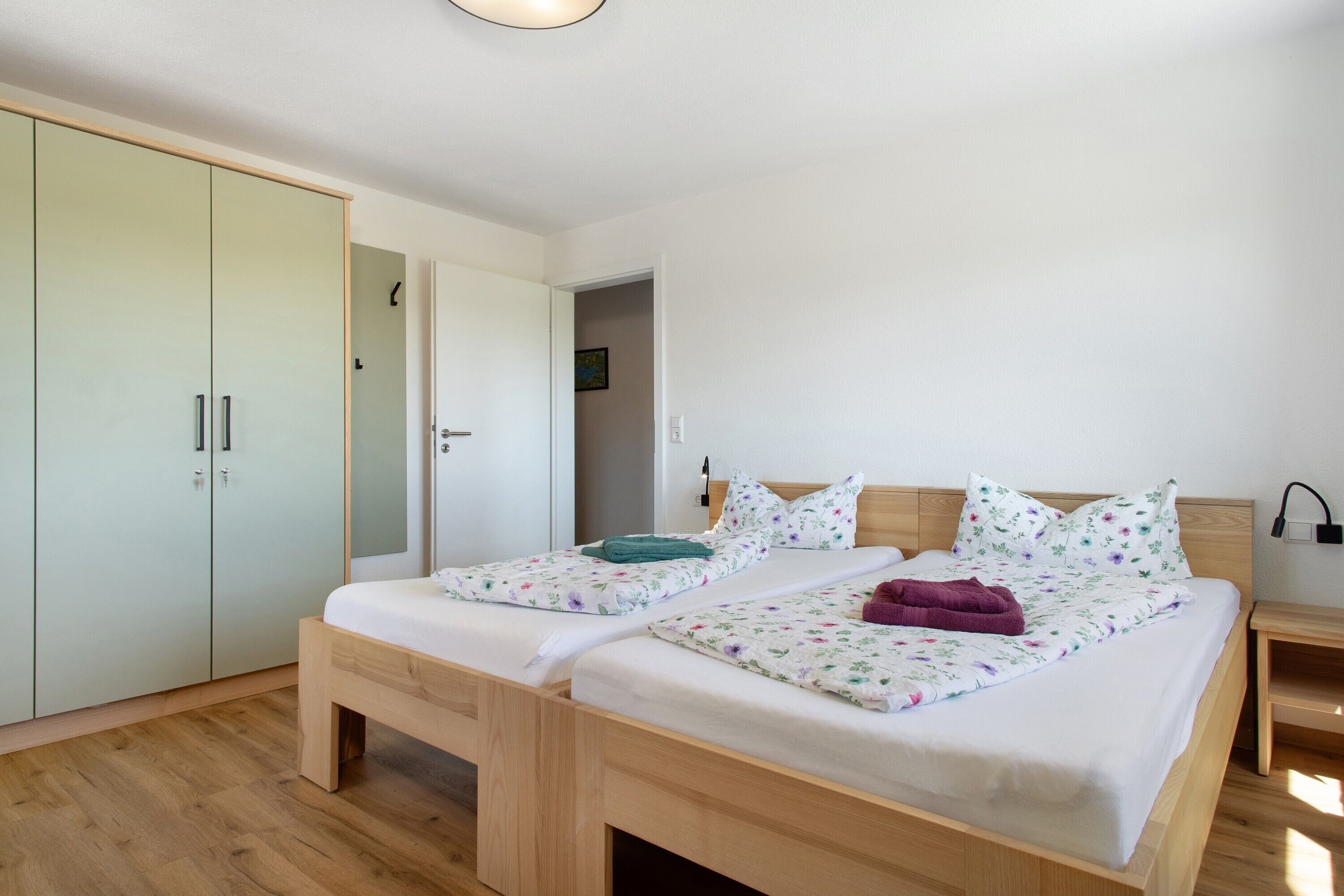 Un dormitorio con dos camas individuales, un armario, una mesita de noche y una puerta que da a otra habitación.
