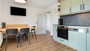 Et moderne køkken med et træspisebord, to stole, et fladskærms-tv og en kaffemaskine.