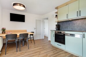 Une cuisine moderne avec une table à manger en bois, deux chaises, un téléviseur à écran plat et une machine à café.