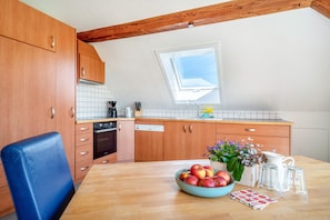 A kitchen with wooden cabinets, a dining table with a bowl of fruit, and a window above the sink. - Apartment 'Säntisblick' with Mountain View and Wi-Fi (Meckenbeuren)