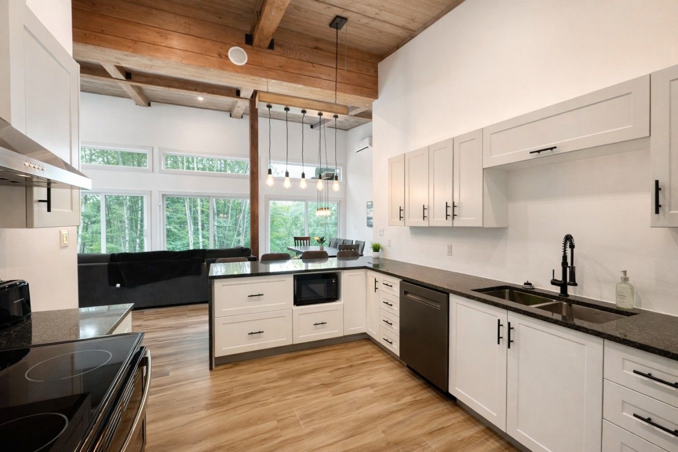 Une cuisine moderne avec des meubles blancs, un plan de travail noir et un plafond en bois.